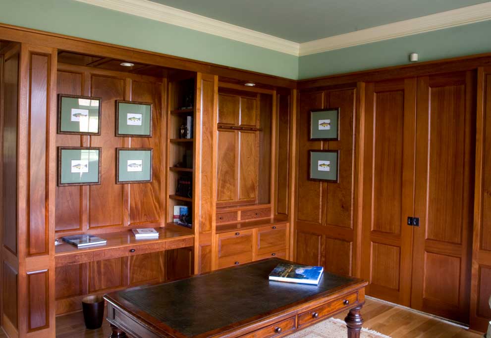 This mahogany study shows a built in back desk with a computer printer hidden in a pullout drawer located below a gun display rack. Pocket doors lead to the master bedroom suite beyond.