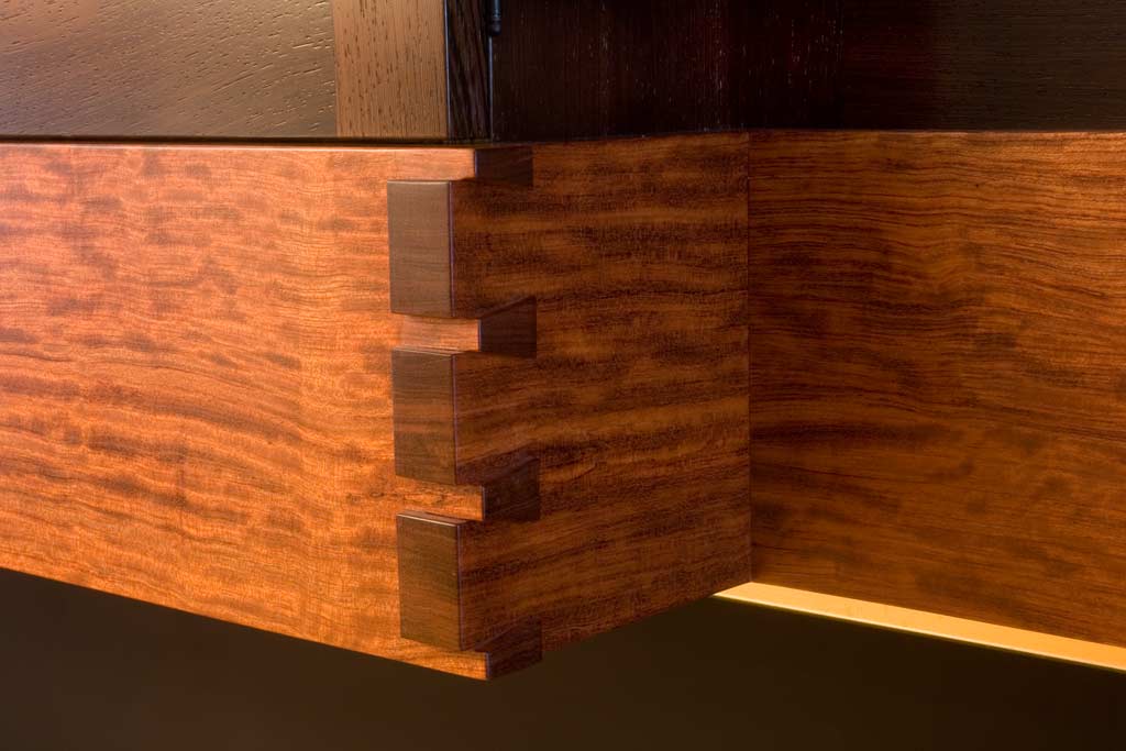 This corner of an entertainment cabinet shows a signature detail of corlis woodworks, the raised dovetail corner. Because of the consummate craftsmanship of the top staff, we can allow craft to be featured. The material here is bubinga, handcut and handsanded.