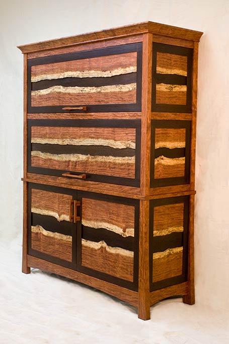 A regular client of ours wanted a special gun cabinet for his son.  They visited the shop and we showed them something we were playing with, using the natural edge of the Bubinga tree, we designed a large gun cabinet to feature the spalted edge of this incredible wood. Normally this is cut off and not used, but it was beautiful and inspired this case.  The dark wood is quarter sawn Wenge.   The two upper doors are barrister style, retracting back into the case to expose pull out gun display racks.